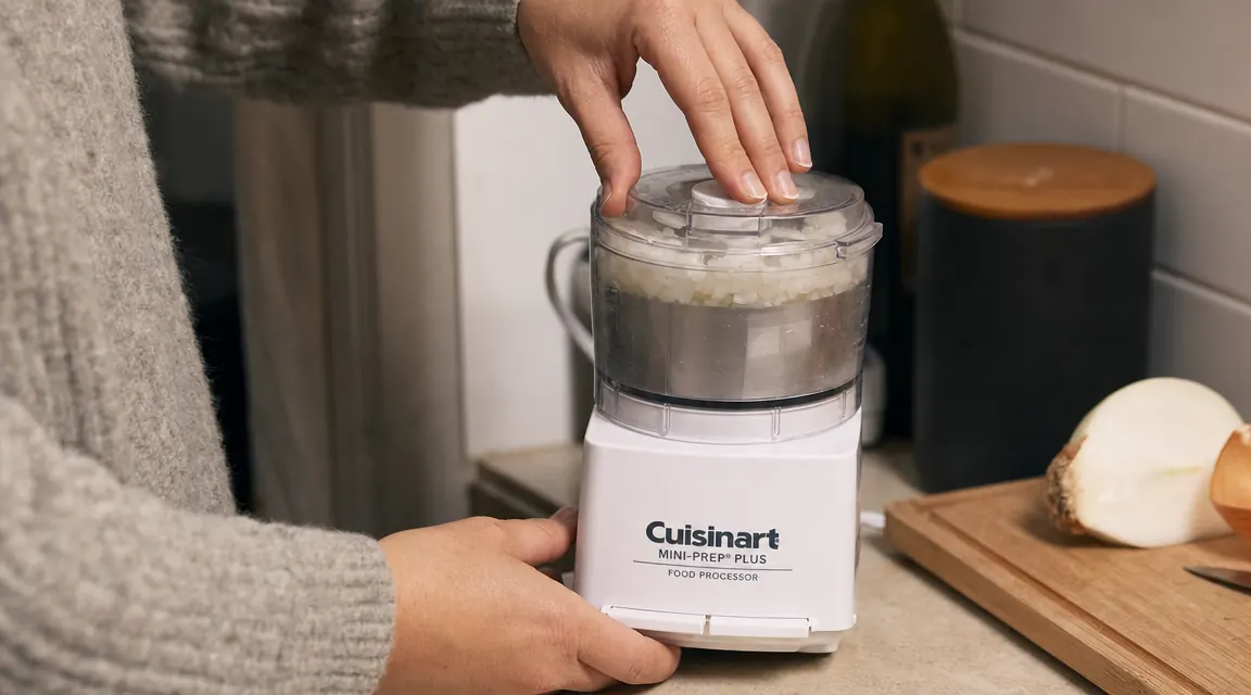 Hand pressing the pulse button on the Cuisinart Mini-Prep Plus with chopped onion visible through the clear lid